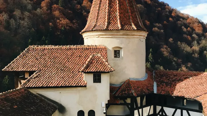 Los tejados y la torre del castillo de Bran con el bosque otoñal al fondo