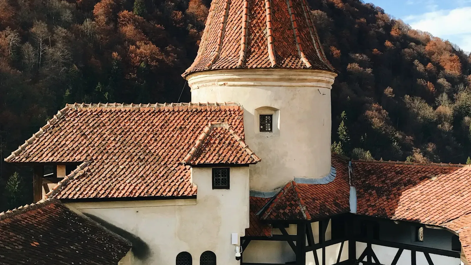 The tiled roofs and tower of Bran Castle with autumn forest behind