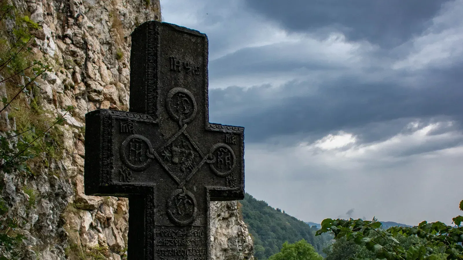 An old carved stone cross below the rock of Bran Castle under a stormy sky