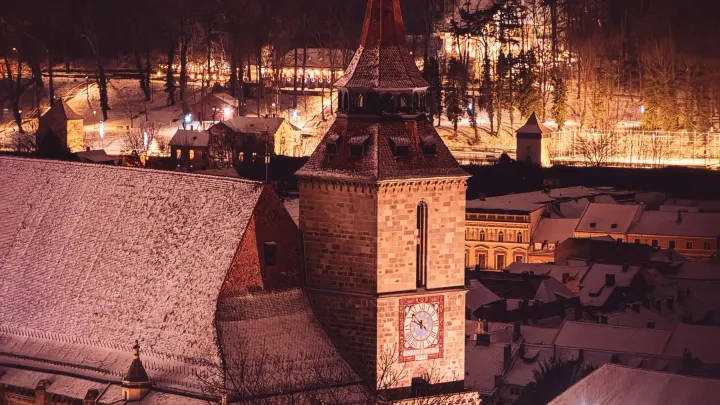 The Black Church and the snowy rooftops of Brașov lit up on a winter night