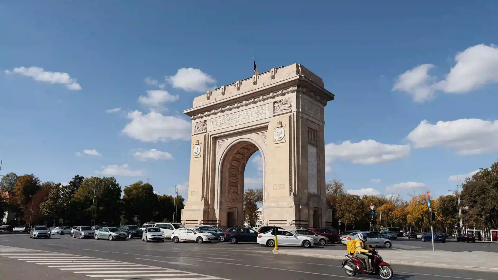 The Arc de Triomphe in Bucharest under a blue sky with autumn trees around the square