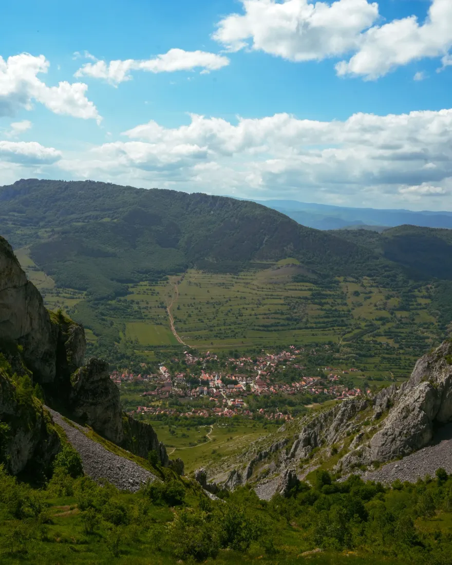 A green mountain valley with a village below forested slopes in the Romanian Carpathians