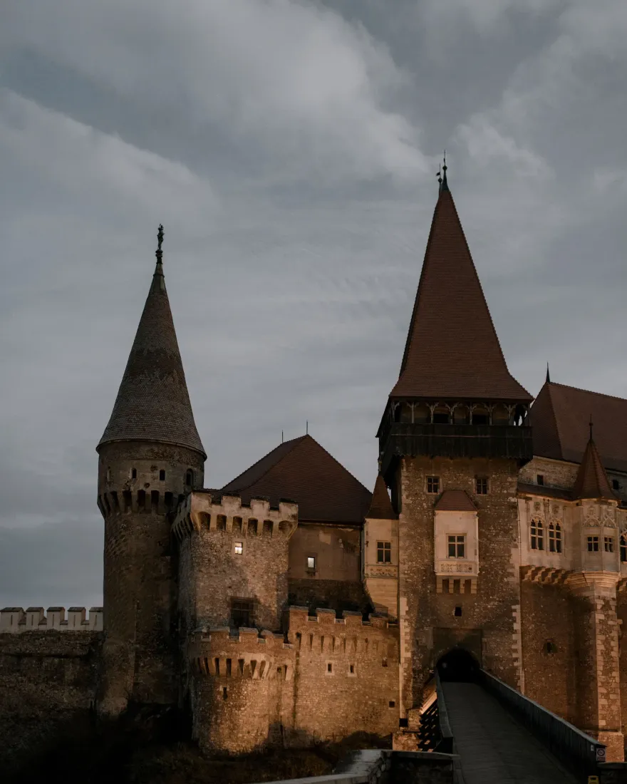 The dark towers of Corvin Castle under a cloudy sky at dusk