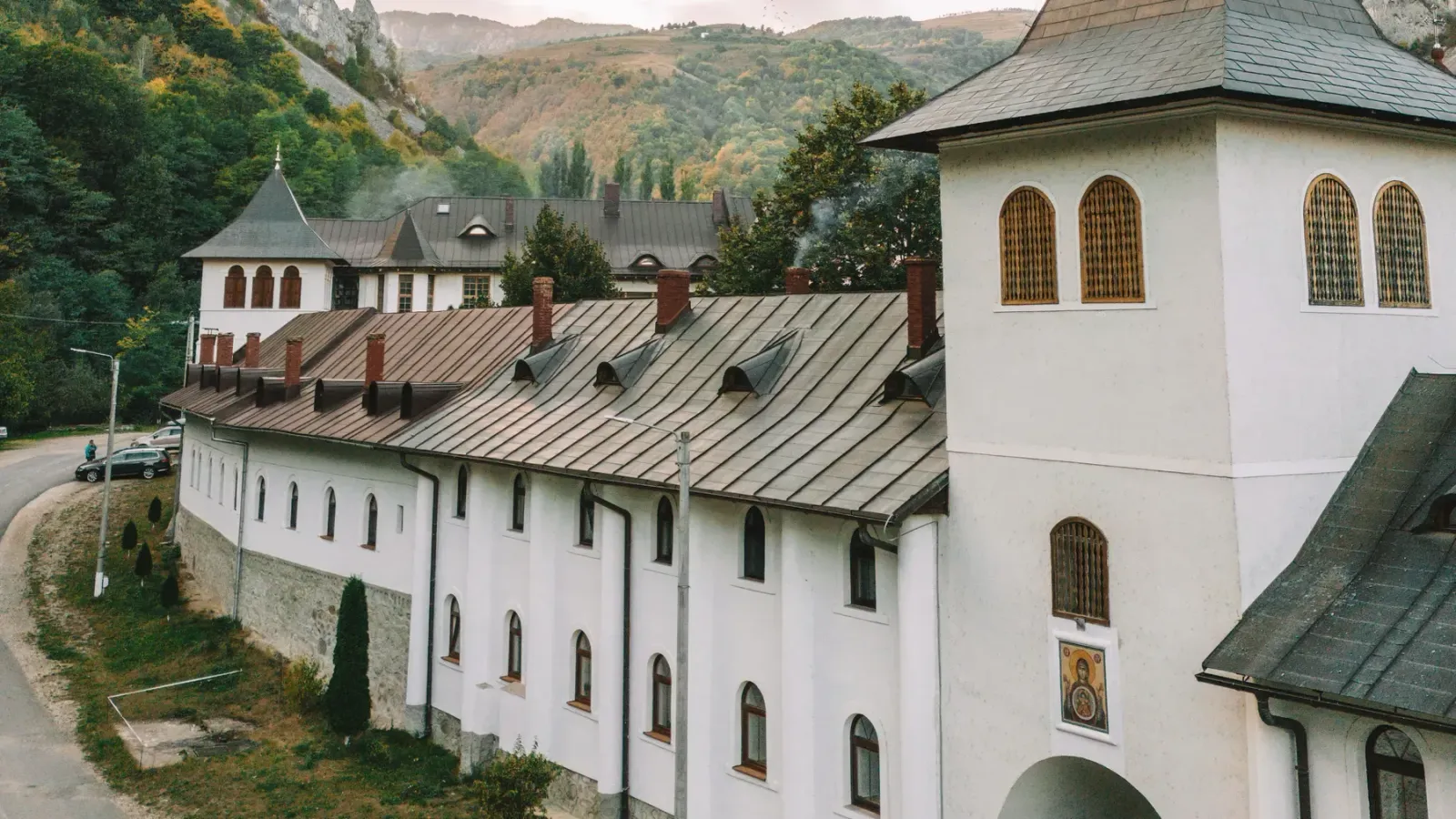 The white walls and tower of a Romanian Orthodox monastery surrounded by forested mountains