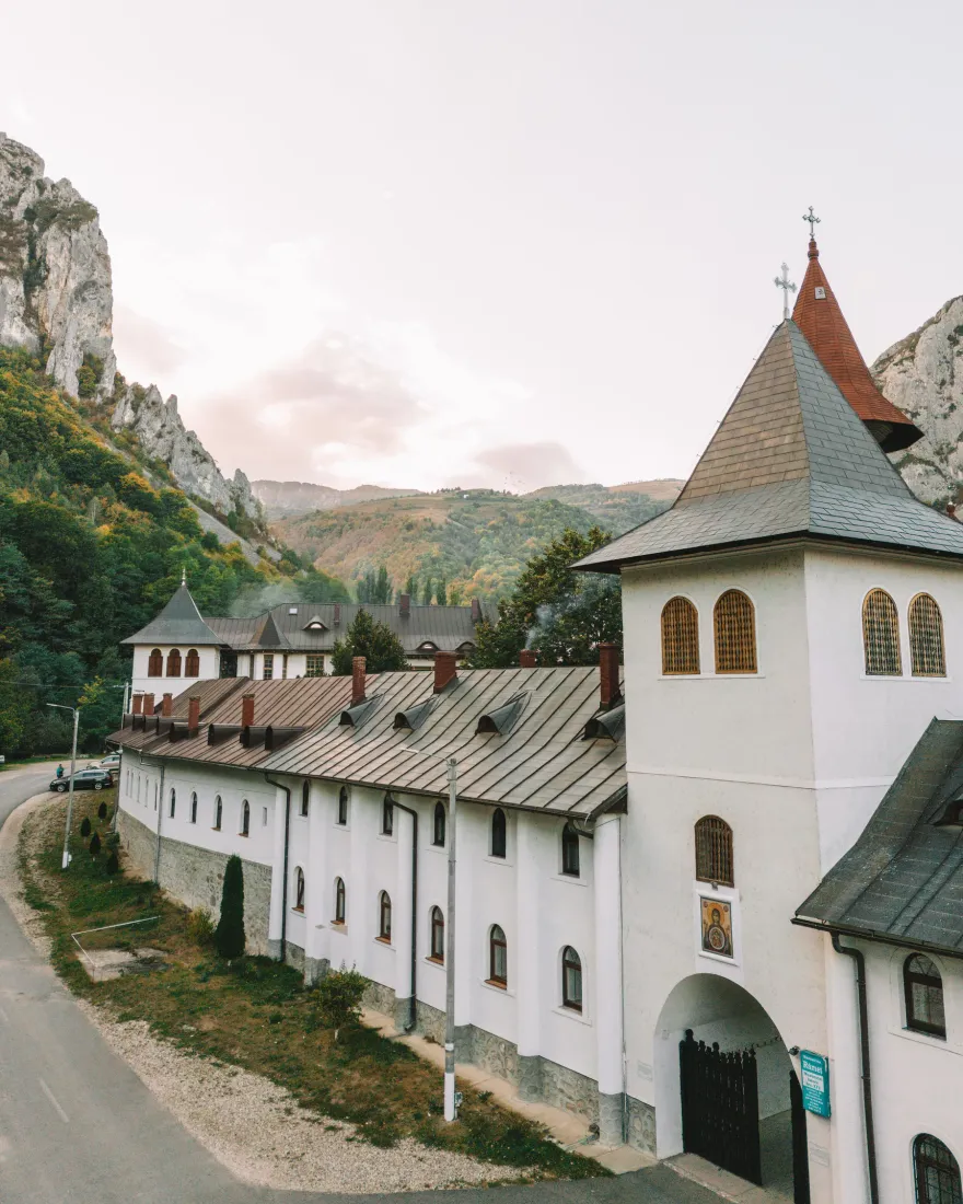 The white buildings and tower of a Romanian monastery below rocky mountains