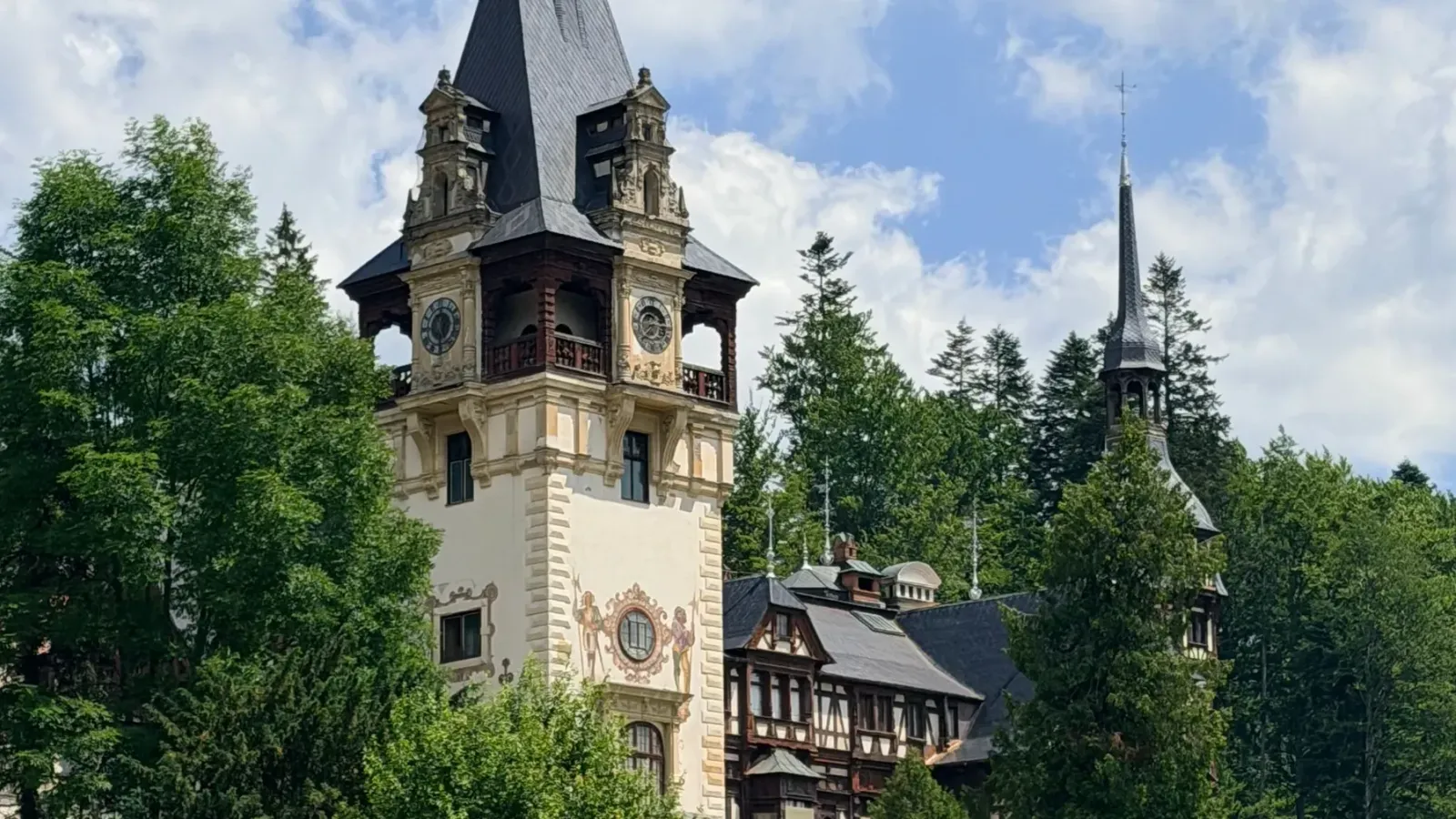 The clock tower and painted facade of Peleș Castle among pine trees in Sinaia