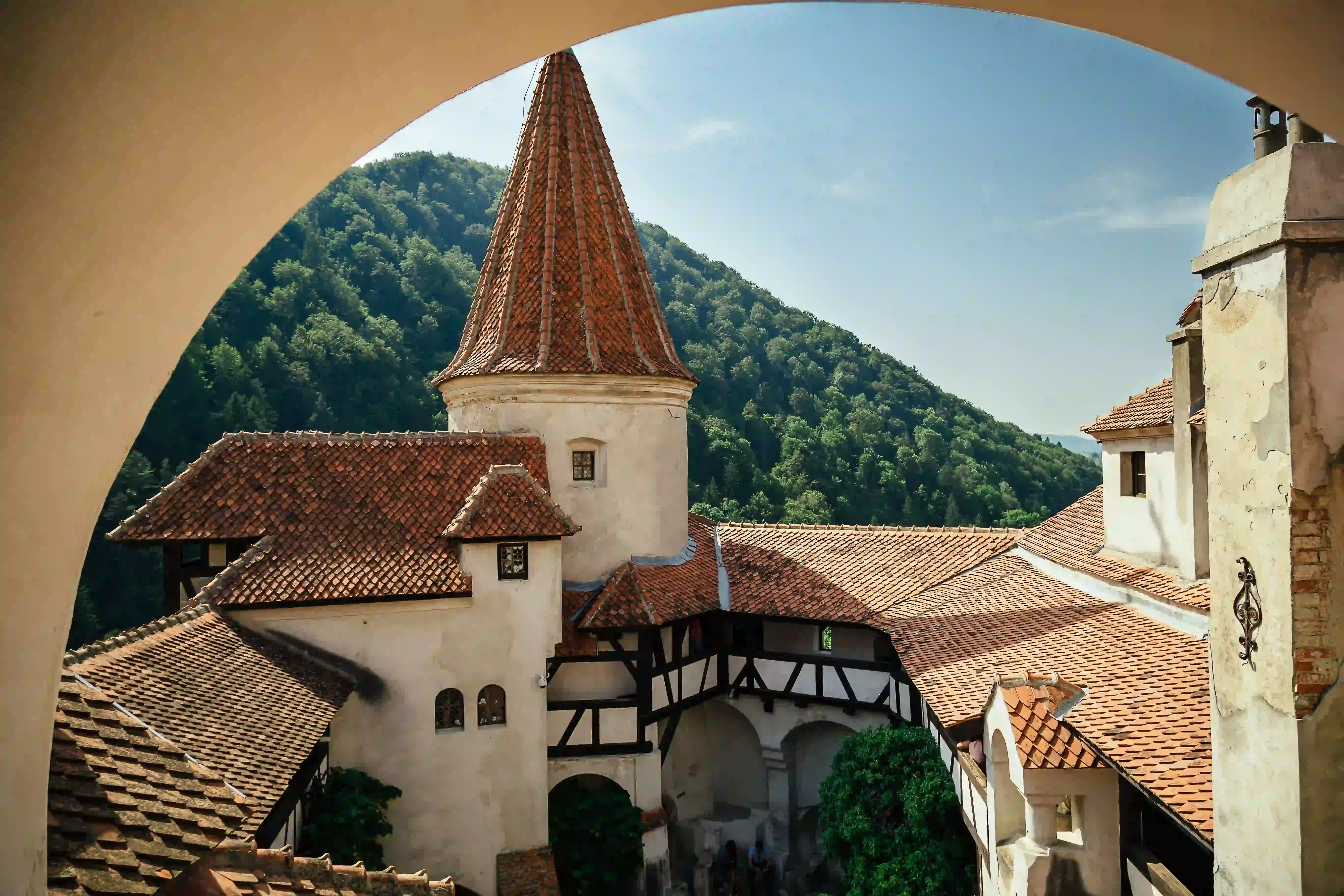 Bran Castle courtyard and tower seen through a stone arch, with forested hills behind