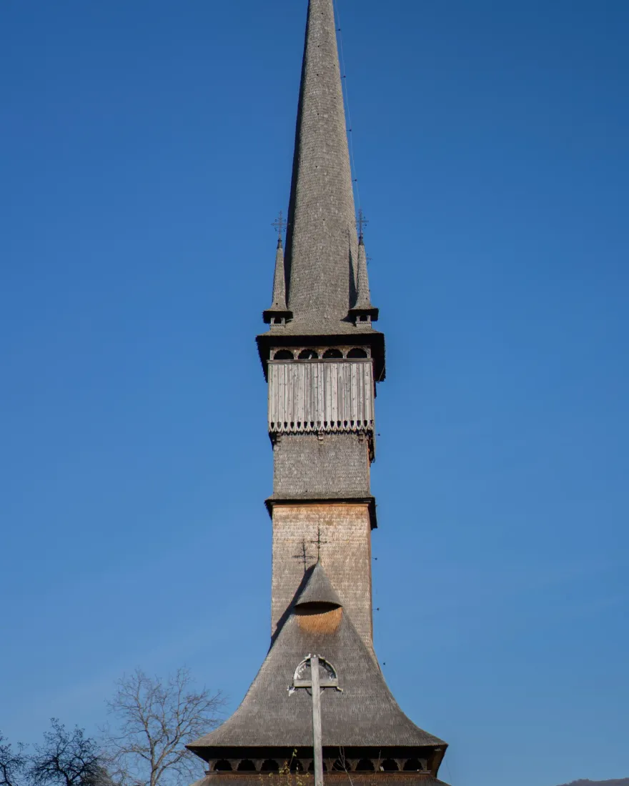 The tall wooden spire of the church of Surdești in Maramureș against a blue sky