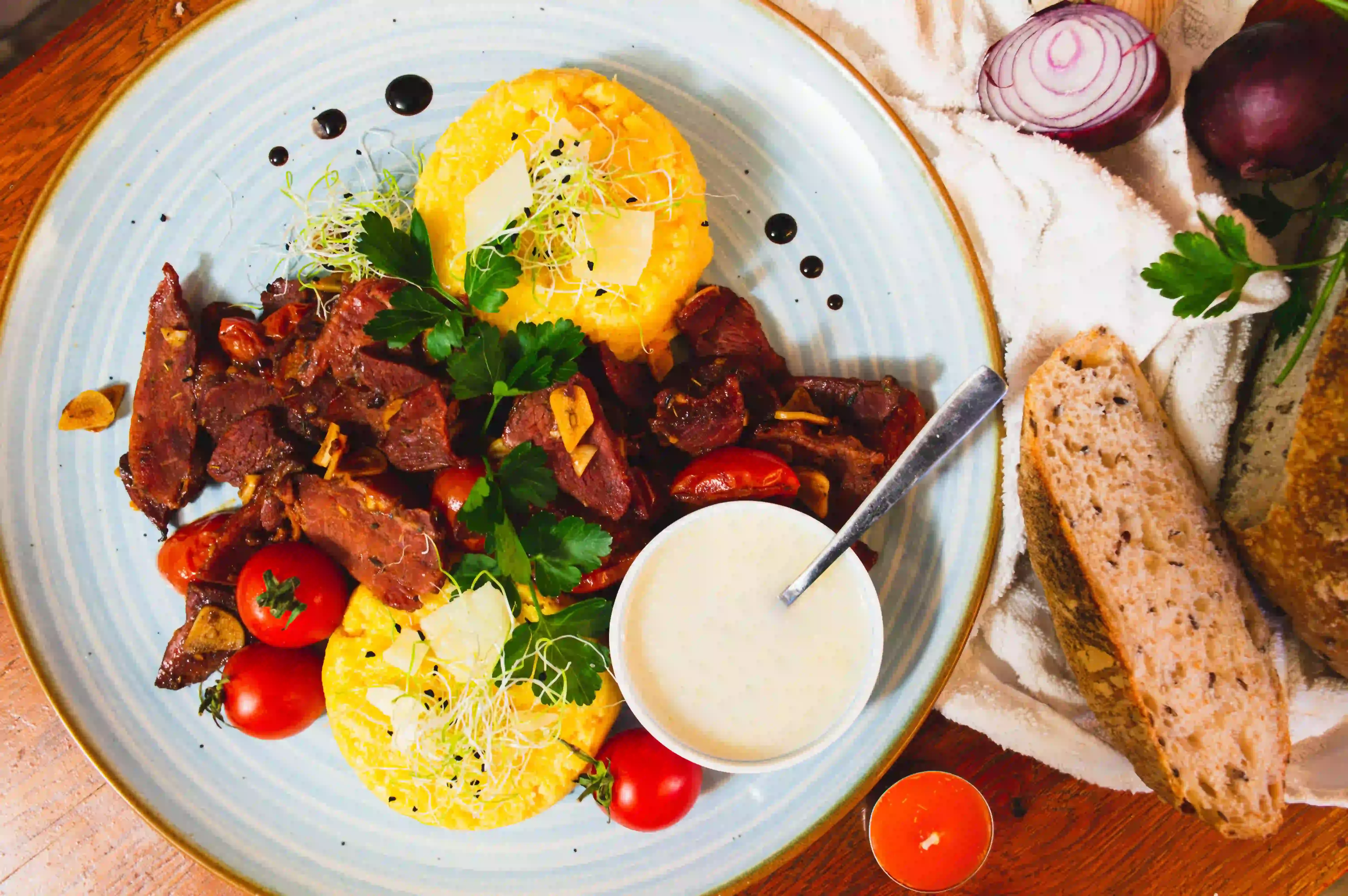 Plate of Romanian food with grilled meat, polenta, tomatoes and sour cream